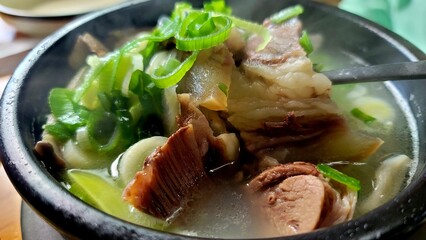 Hot Korean Beef Bone Soup (Gomtang) with green onions and meat served in a stone pot.