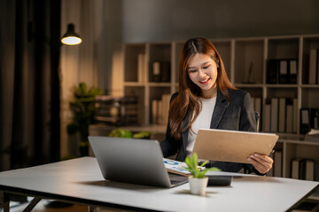 Fototapeta premium Asian businesswoman working late night on laptop with documents