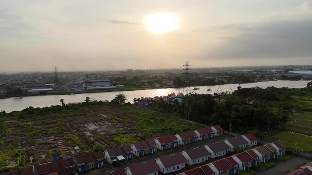 A peaceful evening view with rows of houses along the river, distant industrial landscapes, and tall electricity pylons on the horizon. 