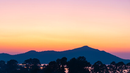 Peaceful mountain landscape at sunrise with colorful pastel sky and soft gradient background. Scenic nature view for travel and tourism concept, calm mood, silhouettes of hills and trees.