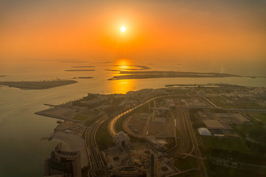 Aerial view of Abu Dhabi, UAE, including Qasr Al Watan and the Corniche. Coastal urban development meets the Persian Gulf during sunset glow.
