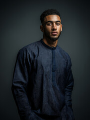 Obraz premium A young man in a dark blue kurta kameez stands confidently in front of a gray background
