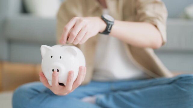 Hand of young Asian man putting coin in piggy bank. Save money and financial investment