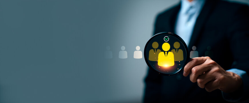 Business professional holding magnifying glass highlighting selected candidate icon, illustrating recruitment screening, talent selection, human resource management, and hiring decision process