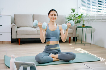 Fototapeta premium Fitness woman exercising with dumbbells at home. Healthy lifestyle, home workout, online fitness training, wellness, strength exercise and modern living concept.
