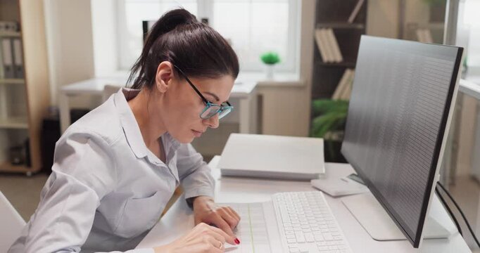 Woman analyst in office typing data spreadsheet. She focuses on a computer monitor to refine a report and validate statistics for financial planning. Focused business data entry and analysis.