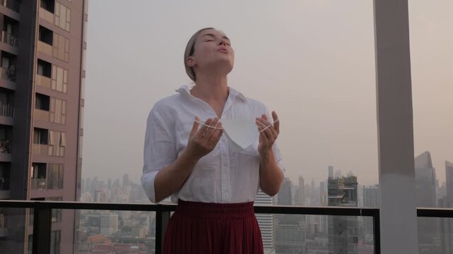 Woman removing face mask and breathing fresh air on rooftop