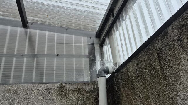 Leaking rain gutter pipe during heavy rainfall, showing drainage problem, water damage risk, and home maintenance issue