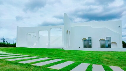 Minimal white modern architecture with arches on green lawn under cloudy sky, clean lines and serene atmosphere.