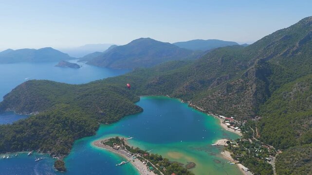 Oludeniz, Turkey. Aerial view of a paraglider with red parachute descending over Blue Lagoon, Oludeniz Beach and green mountains, Babadag Mountain in background, summer.. Aerial View