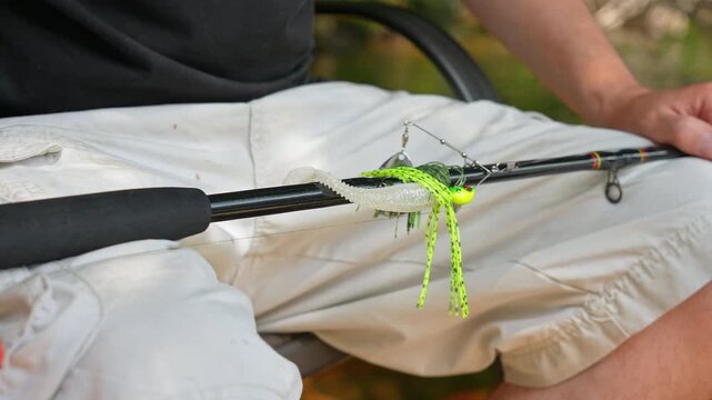 Man sitting with casting rod and attached perch spinner spoon blade with plastic paddle tail bait lure minnow to metal leader with braid for big bass or pike fishing. Sport fishing charter.