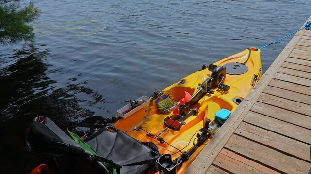 Fully rigger kayak watercraft mooring and tied to boat pier near cottage. Recreational watercraft, kayaking lake during tournament or fishing derby. Kayak water craft equipment for fishing activities.