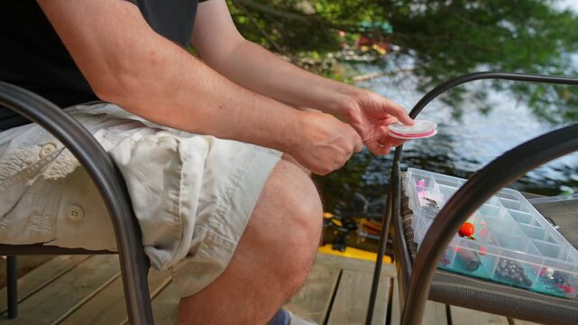 Angler hobbyist pulling fluorocarbon leader to fix tackle with fishing hook, line and lure or bait. Sport fishing. Man enjoys fishing at summer vacation. Peaceful water setting near cottage.