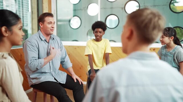 Smart teacher talking about mental health problem and sharing idea with boy during group therapy. Happy instructor pointing at children while explain plan while student listening idea. Edification