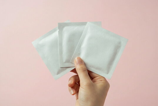 Hand holding three small white facial mask , sashet set, cosmetic products packaging blank mockup on pale pink background.  Product presentation. Space for text and logo