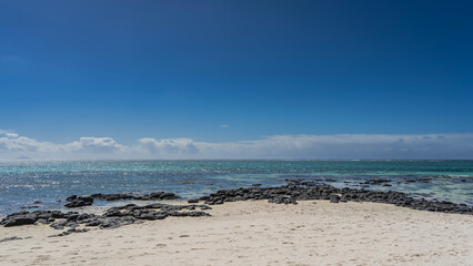 The beach of a tropical island. Footprints in the white sand. Black volcanic boulders near the water. A calm turquoise ocean. Blue sky, clouds. Mauritius. Belle Mare. © Вера 