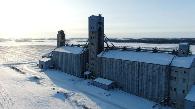 Aerial view of a large grain elevator complex in a snowy rural landscape under a clear winter sky