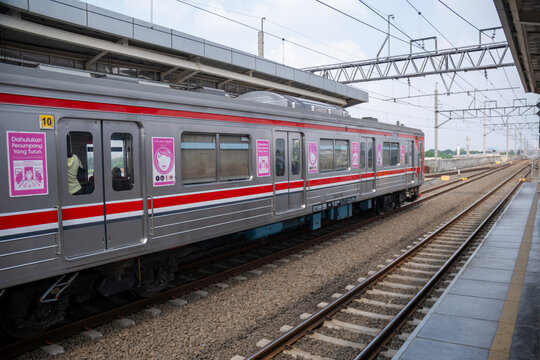 Jakarta, Indonesia - May 12, 2024 : A KRL Commuterline train stops at an elevated station platform. The silver railcar features red stripes and pink stickers designating women-only carriages