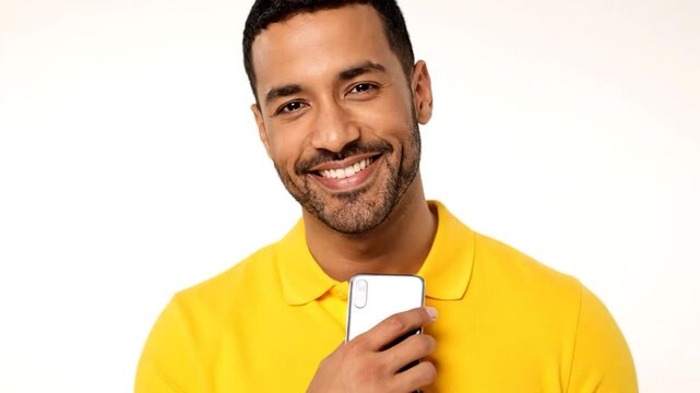 Smiling man holding a smartphone, wearing a yellow collared shirt against a white backdrop