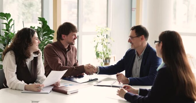 Group of business people handshaking during formal meeting in office. Two Caucasian businessmen sit at conference table, shaking hands, conclude agreement, establish partnership. Negotiations, deal