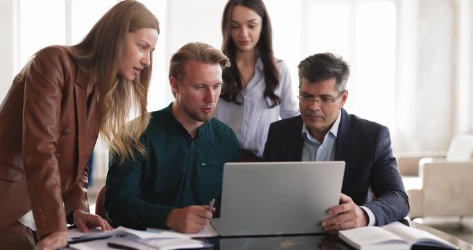Diverse team of professionals gathered around laptop during collaborative business meeting, review digital data, analyze project results, make strategic decisions in office. Teamwork, modern workflow