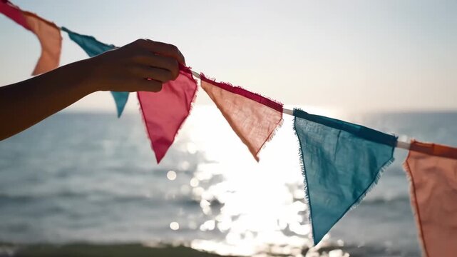 Colorful Flags at the Seaside - A hand holds up a string of colorful triangular fabric flags in pink, peach, and blue tones.