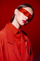 Young woman styled in bold red fashion and vibrant makeup, wearing orange sunglasses in a creative...