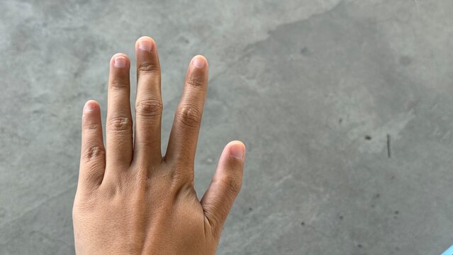 A hand with fingers spread open, showing short natural nails and light brown skin. The background is a gray concrete surface, creating a simple and natural mood
