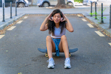 Fototapeta premium Young woman with headphones on a skateboard relaxing on an urban street