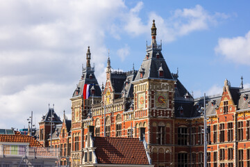 Naklejka premium Iconic Amsterdam central station historical building with dutch flag in The Netherlands.