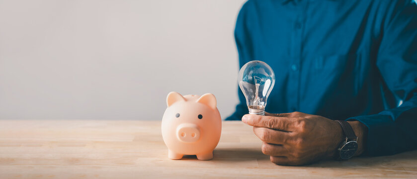 Man holding light bulb next to piggy bank for financial innovation, money saving, investment idea, energy efficiency, retirement planning, smart finance goals, future market growth