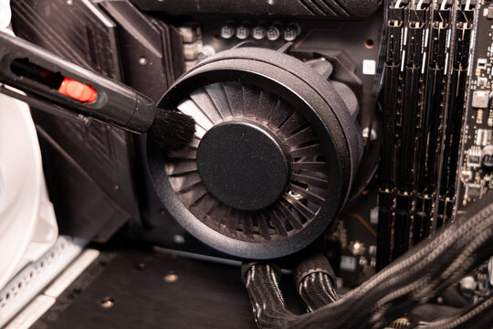Technician hand cleaning black CPU fan blades with a brush for better computer performance