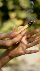 A close-up of a woman's hands holding a smoking palo santo stick while performing a magical ritual against a green forest backdrop.