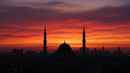 Obraz premium Silhouetted mosque at sunset with vibrant skies and city skyline in the background