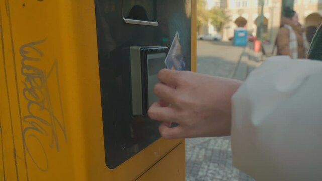 A close-up of a hand using a card at a payment kiosk in an urban setting, showcasing digital payment technology in everyday life.