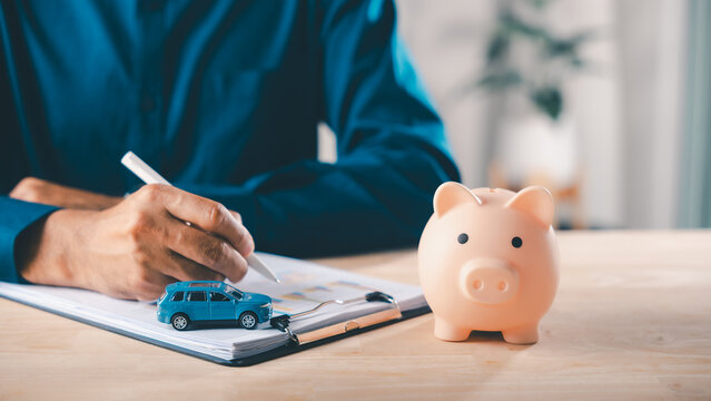 Man signs car finance contract near piggy bank, as money insurance and auto lease price help save documents and savings for bank loan and vehicle purchase planning process