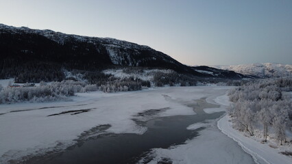 Obraz premium Winter landscape with frozen river and snow-covered mountains in Norway during late afternoon