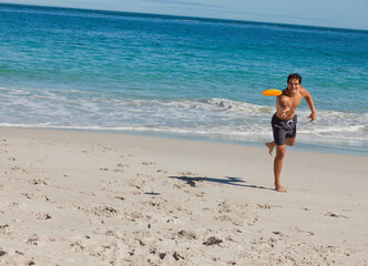 Adult man running on beach throwing orange disc in swim trunks white string, footprints, copy space