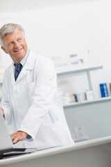 Senior medical professional wearing white lab coat, pen-pocket, using laptop at counter, copy space