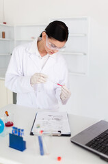 Transparent test tube holding red liquid is resting on white lab bench near laptop