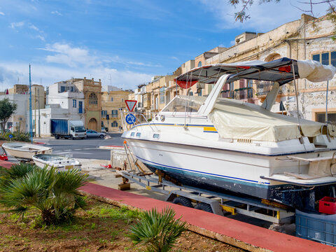 Birzebbuga, Malta &ndash; boat on trailer at roadside, Mediterranean old buildings in the background and blue sky with sunshine