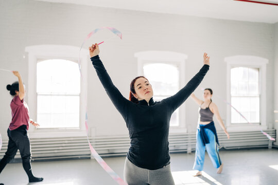 Woman raises ribbon high during group dance practice in studio