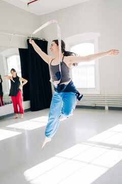 Dancer leaping with rhythmic gymnastics ribbon in modern studio