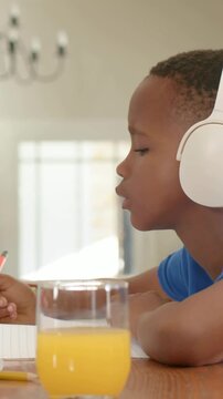 Vertical video: Song starting, boy in blue shirt white headset singing at table, writing homework