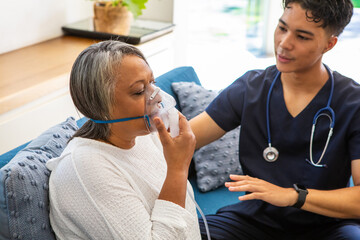 Senior african american woman using oxygen mask, asian nurse in scrubs guiding © wavebreak3