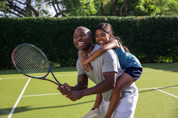 African American father and Asian child daughter holding racket while piggybacking on tennis court © wavebreak3