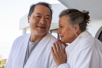 Obraz premium Diverse senior couple standing on spa balcony, wearing bathrobes and gazing at each other