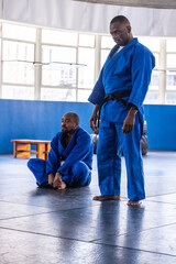 African american martial arts partners practicing kicks on mats in blue gis, copy space