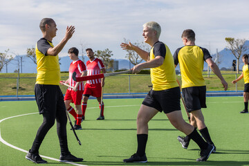 Fototapeta premium Male athletes high-fiving on synthetic turf in yellow jerseys and holding field hockey sticks