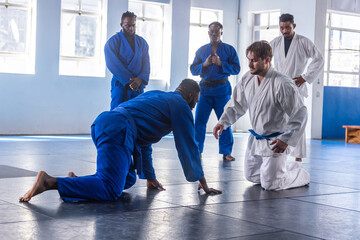 Diverse martial arts students in gis, belts practicing grappling on padded mat in studio